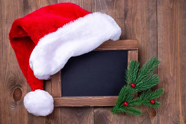 Placa de giz vazia ou quadro-negro com chapéu de Papai Noel e galhos de árvore de Natal, espaço de cópia horizontal — Fotografia de Stock