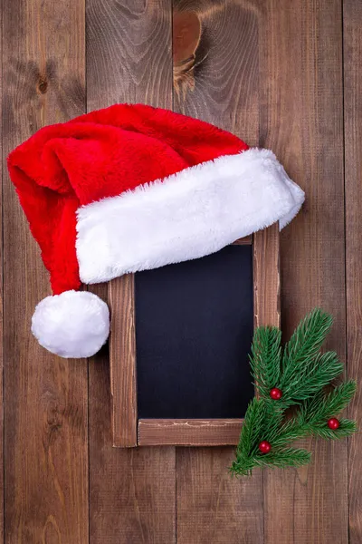 Leere Kreidetafel oder Tafel mit Weihnachtsmütze und Weihnachtsbaumzweigen, Kopierraum vertikal — Stockfoto