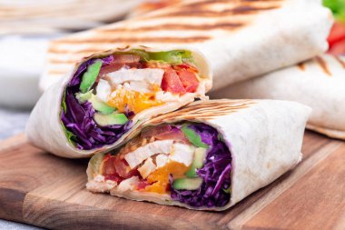 Ahşap tahtanın üzerinde kızarmış tavuk, lahana, avokado, domates, marul ve çedar peyniri.