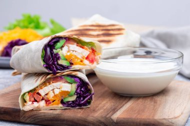 Ahşap tahtanın üzerinde kızarmış tavuk, lahana, avokado, domates, marul ve çedar peyniri.