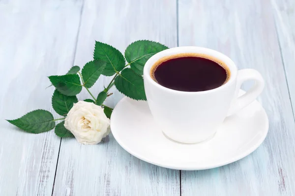 Café oscuro en taza blanca, hermosa rosa sobre fondo, mesa de madera azul claro, horizontal — Foto de Stock