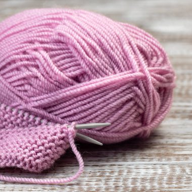 İğneli örgü parçası ve ahşap arka planda pembe iplik kesesi, kare biçiminde.