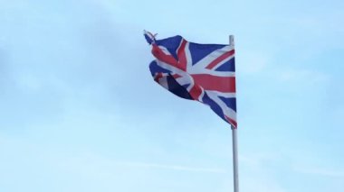 Lightly battered British flag waving in wind on blue sky background, Union Flag or Union Jack. High quality 4k footage