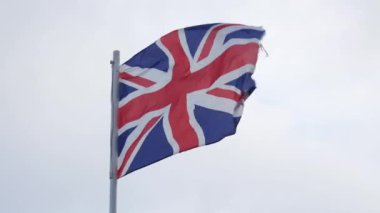 Lightly battered British flag waving in wind on gray sky background, Union Flag or Union Jack closeup. High quality 4k footage