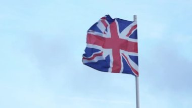 British flag waving in wind on blue sky background, Union Flag or Union Jack. High quality 4k footage