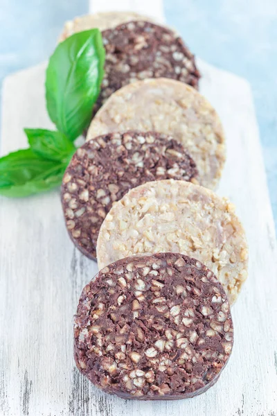 Traditional Irish and British black pudding and white or oatmeal pudding sausage on a wooden board, vertical