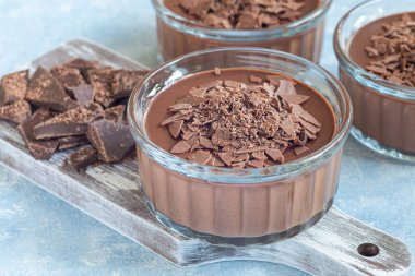 Çikolatalı Panna Cotta tatlı içinde cam ramekin, ahşap tahta ve kırık çikolata arka plan, yatay