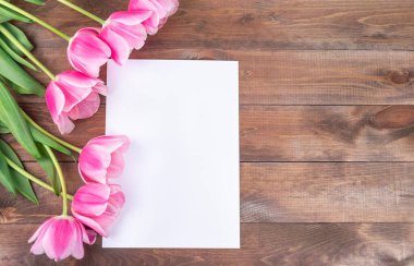 Güzel pembe laleler ve kahverengi ahşap arka planda beyaz bir kağıt parçası, Anneler Günü için tebrik kartı, 8 Mart veya Sevgililer Günü konsepti, yatay, fotokopi alanı, üst görünüm