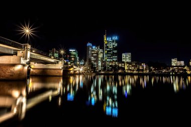 Frankfurt 'un ufuk çizgisi, geceleri soğuk bir kış günü suda renkli yansımalarla ana cadde. Uzun pozlama olarak alınır.