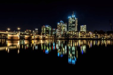 Frankfurt 'un ufuk çizgisi, geceleri soğuk bir kış günü suda renkli yansımalarla ana cadde. Uzun pozlama olarak alınır.