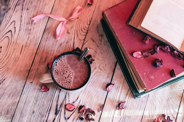 Bir fincan sıcak çikolata, mis kokulu gül yaprakları ve ahşap masada eski kitaplar. Vintage filtre biçimi