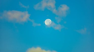 Mavi gökyüzünde ay sabah bulutlarla çevrili.