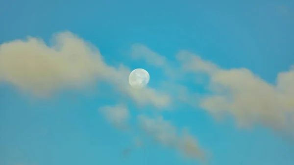 Moon on the blue sky behind clouds in the morning