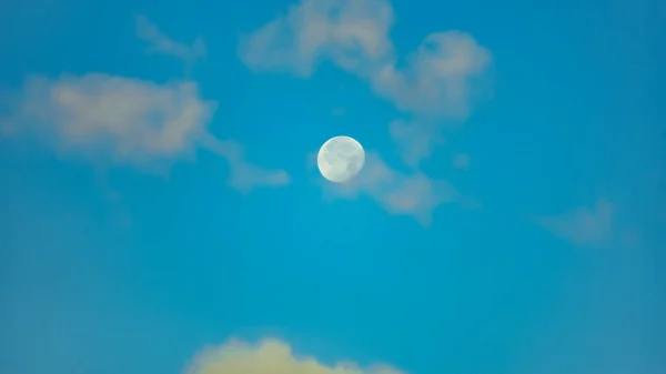 Mavi gökyüzünde ay sabah bulutlarla çevrili.