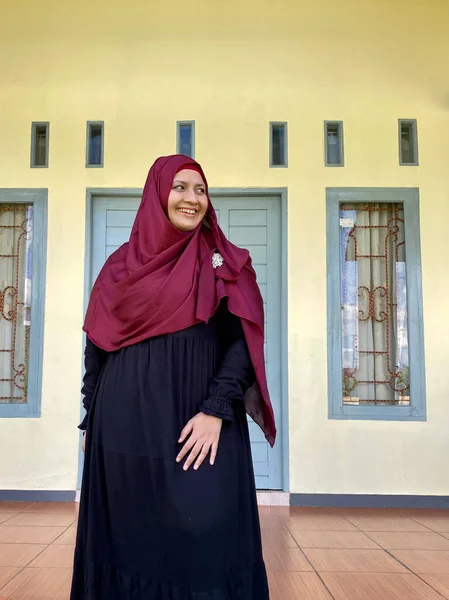 Asian woman wearing red hijab looking away smiling in front of house