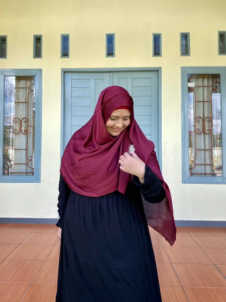 Asian woman wearing red hijab looking away smiling in front of house