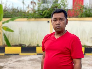 Young man in red shirt standing alone in front of house