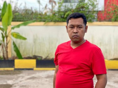 Young man in red shirt standing alone in front of house