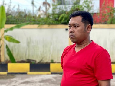 Young man in red shirt standing alone in front of house