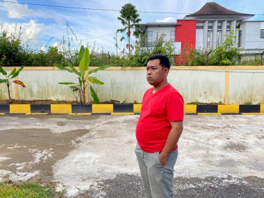 Young man in red shirt standing alone in front of house
