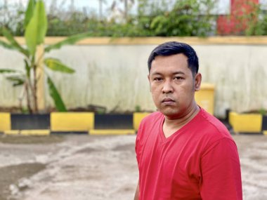 Young man in red shirt standing alone in front of house