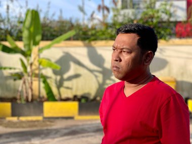 Young man in red shirt standing alone in front of house