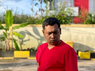 Young man in red shirt standing alone in front of house