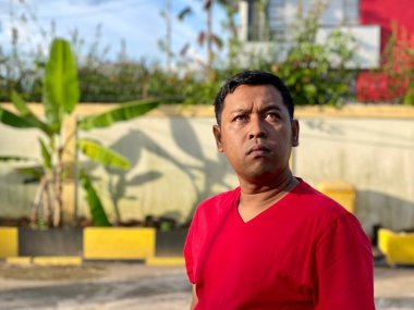 Young man in red shirt standing alone in front of house