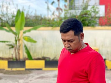 Young man in red shirt standing alone in front of house