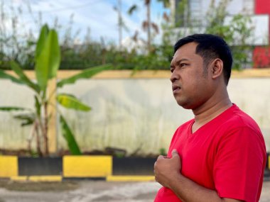 Young man in red shirt standing alone in front of house