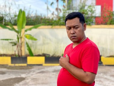 Young man in red shirt standing alone in front of house