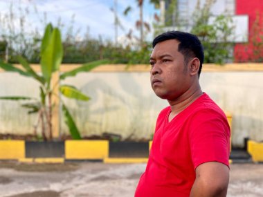 Young man in red shirt standing alone in front of house