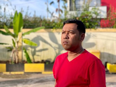 Young man in red shirt standing alone in front of house