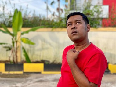 Young man in red shirt standing alone in front of house