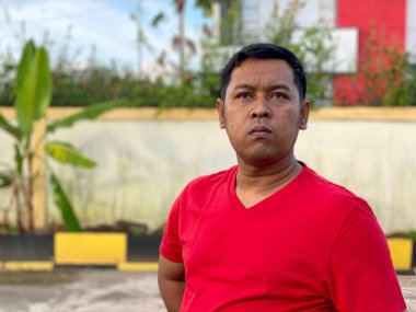 Young man in red shirt standing alone in front of house