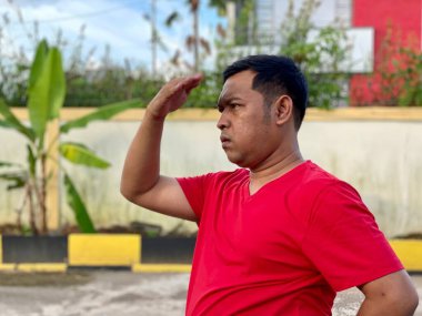 Young man in red shirt standing alone in front of house