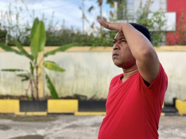 Young man in red shirt standing alone in front of house