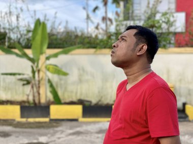 Young man in red shirt standing alone in front of house