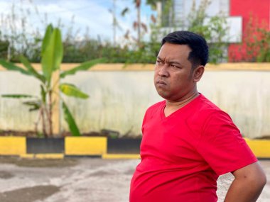 Young man in red shirt standing alone in front of house