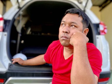 The young man in the red shirt squats in the back of the car
