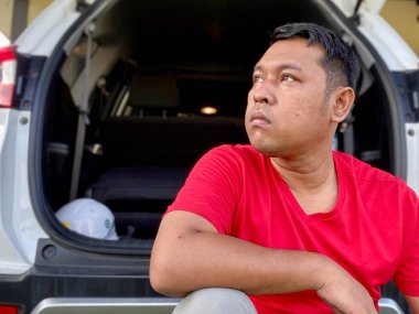 The young man in the red shirt squats in the back of the car