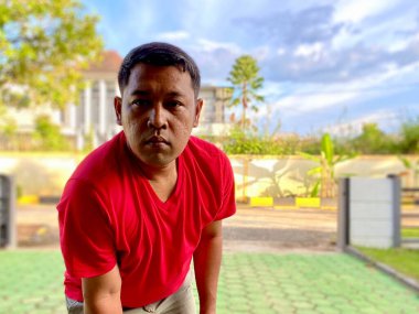 The young man in the red shirt squats in the yard