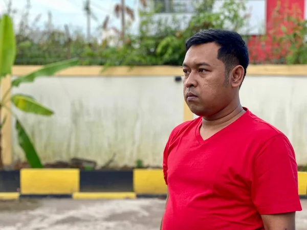 Young man in red shirt standing alone in front of house