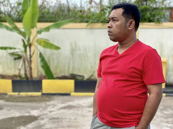 Young man in red shirt standing alone in front of house