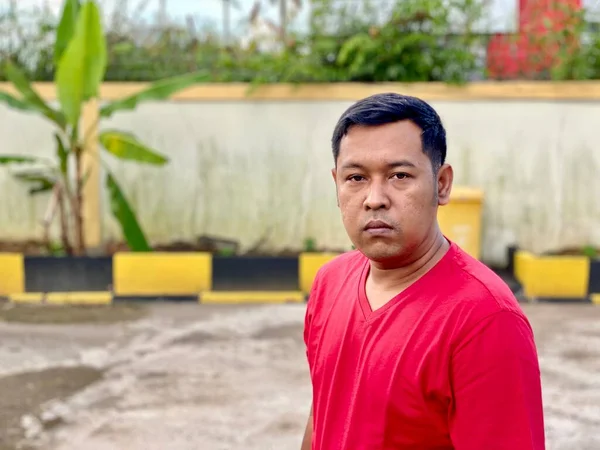 Young man in red shirt standing alone in front of house