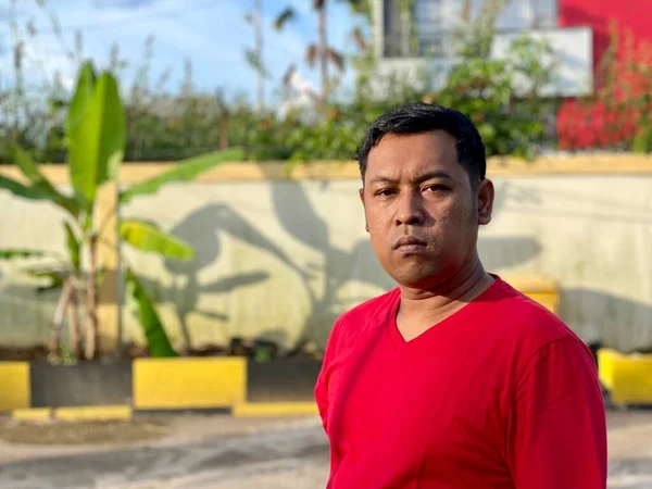 Young man in red shirt standing alone in front of house
