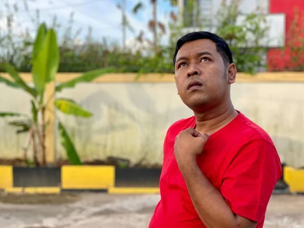 Young man in red shirt standing alone in front of house