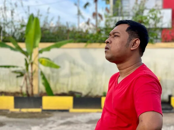 Young man in red shirt standing alone in front of house