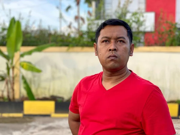 Young man in red shirt standing alone in front of house