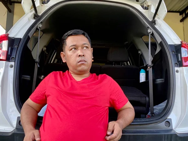 The young man in the red shirt squats in the back of the car